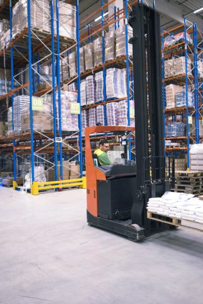 worker-operating-forklift-machine-and-relocating-goods-in-large-warehouse-center-min